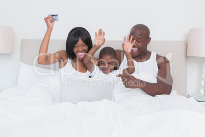 Happy smiling pretty couple using laptop with his son in bed