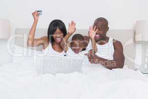 Happy smiling pretty couple using laptop with his son in bed
