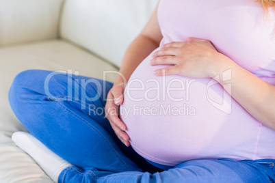 Close up of pregnant woman sitting on couch touching her belly