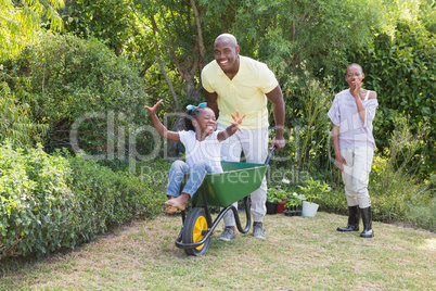 Happy smiling couple playing with wheelbarrow and their daughter