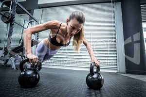 Muscular woman doing pushups with kettlebells