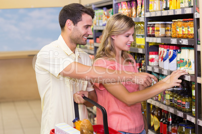 Smiling bright couple buying food products showing shelf