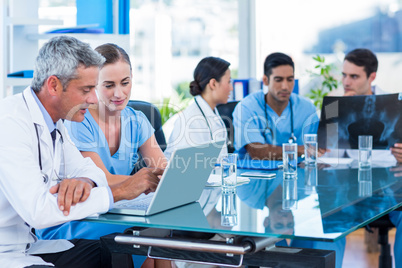 Doctor and nurse looking at laptop with colleagues behind