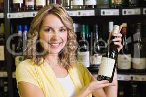 Portrait of a smiling pretty blonde woman showing a wine bottle