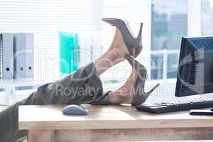 Businesswoman sitting on swivel chair with feet on desk