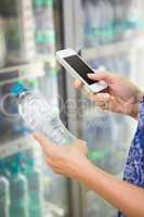 Woman comparing the price of a bottle of water with her phone