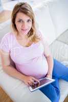 Pregnant woman looking at camera and using tablet