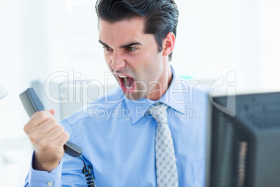 Businessman shouting as he holds out phone at office