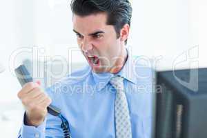 Businessman shouting as he holds out phone at office
