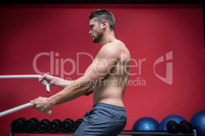 Muscular man exercising with rope