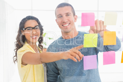 Portrait of smiling coworkers pointing sticky notes and looking