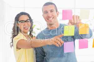 Portrait of smiling coworkers pointing sticky notes and looking