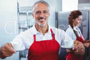Smiling barista holding cups of coffee with colleague behind