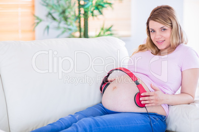 Smiling pregnant woman putting headphones on her belly