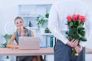 Businessman hiding flowers behind back for colleague