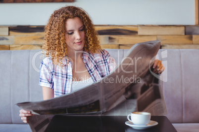 Pretty curly hair girl having cup of coffee and reading newspape