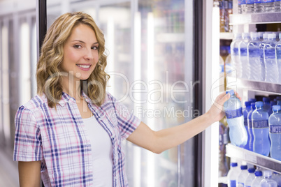 Portrait of a smiling pretty blonde woman taking a water bottle