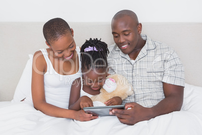 Pretty couple using tablet with their daughter in bed