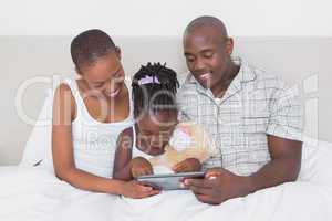 Pretty couple using tablet with their daughter in bed