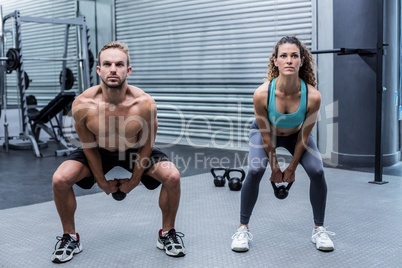 A muscular couple lifting kettlebells