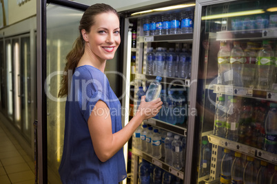 Pretty woman taking bottle of water in fridge