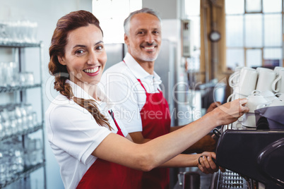Smiling barista using the coffee machine with colleague behind