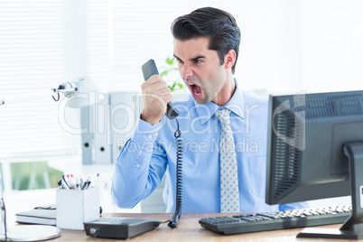 Businessman shouting as he holds out phone at office