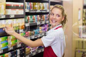 Smiling blonde worker taking a product in shelf