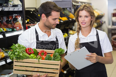 Two colleagues holding a box with fresh vegetables and writing o