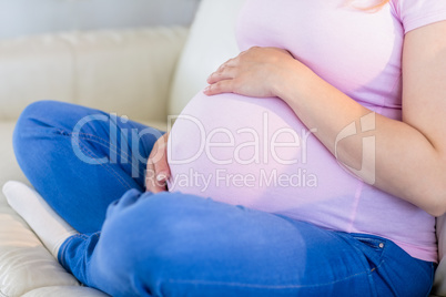 Close up of pregnant woman sitting on couch touching her belly