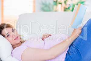 Pregnant woman looking at camera and reading a book