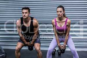 A muscular couple lifting kettlebells