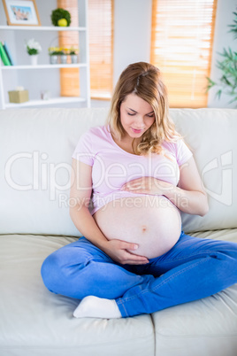 Pregnant woman sitting on couch touching her belly