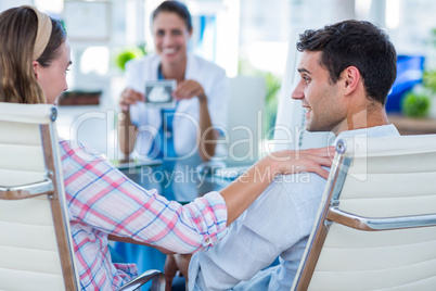 Rear view of pregnant woman and her husband discussing with doct