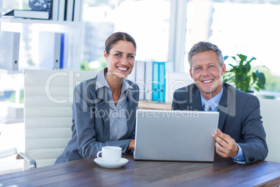 Business people looking at camera and using laptop