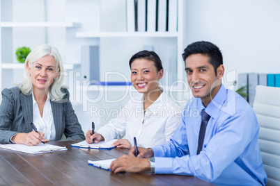 Business people writing on clipboards and looking at camera