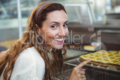 Pretty brunette pointing at pastries through the glass