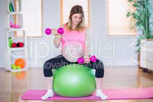 Pregnant woman lifting dumbbells on exercise ball