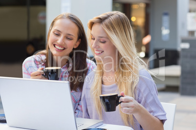 Happy women friends drinking coffee and looking at laptop