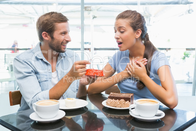 Young happy couple eating cake and man giving her a ring