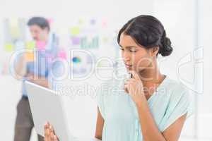 Businesswoman working on laptop screen with colleague behind her