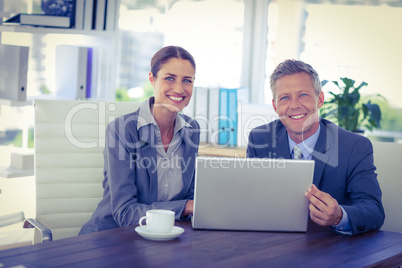 Business people looking at camera and using laptop