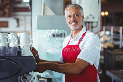Happy barista smiling at camera and using the coffee machine
