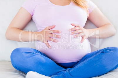 Close up of pregnant woman sitting on couch touching her belly