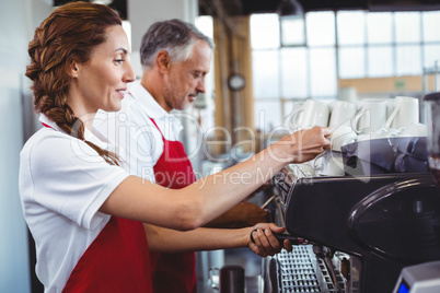 Pretty barista using the coffee machine with colleague behind