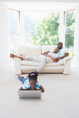 Pretty couple sitting on couch and their daughter using laptop