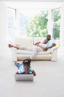 Pretty couple sitting on couch and their daughter using laptop