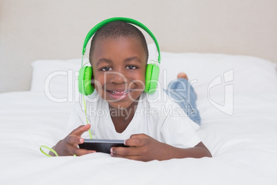 Portrait of a pretty little boy using smartphone and listening m