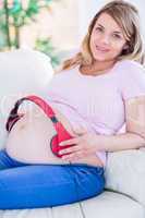 Smiling pregnant woman putting headphones on her belly