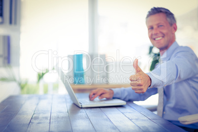 Happy businessman using laptop computer and looking at camera wi